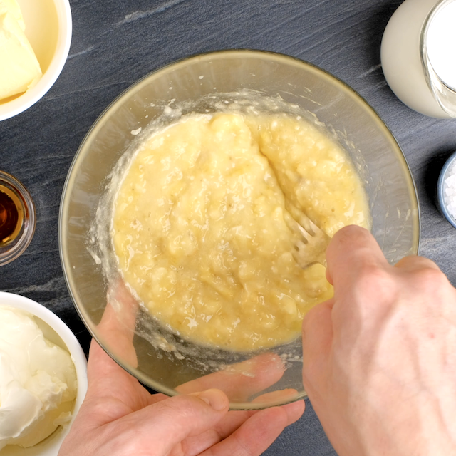 Bananas being mashed to make banana cake with cream cheese frosting.