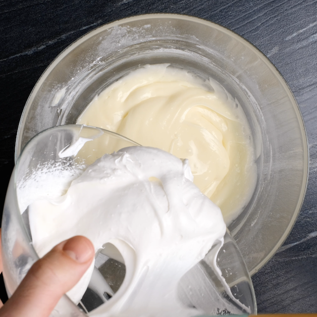 Whipped heavy cream being added to cream cheese mixture to make cream cheese frosting for banana cake.