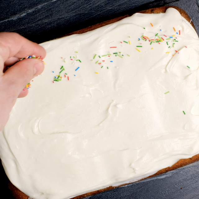Sprinkles being added to cream cheese frosting on banana cake.
