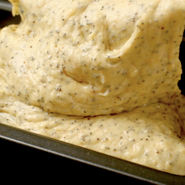 Lemon poppy seed bread batter being poured into a greased loaf pan.