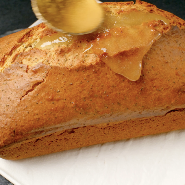 Glaze being poured over freshly baked lemon poppy seed bread.