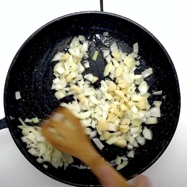 Onions and garlic being sautéed in a pan to make lemon salmon pasta at home.