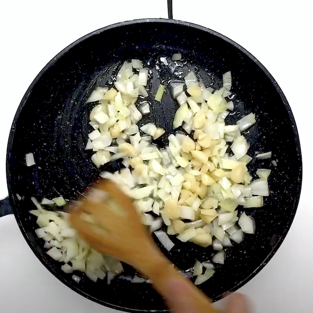 Onions and garlic being sautéed in a pan to make lemon salmon pasta at home.