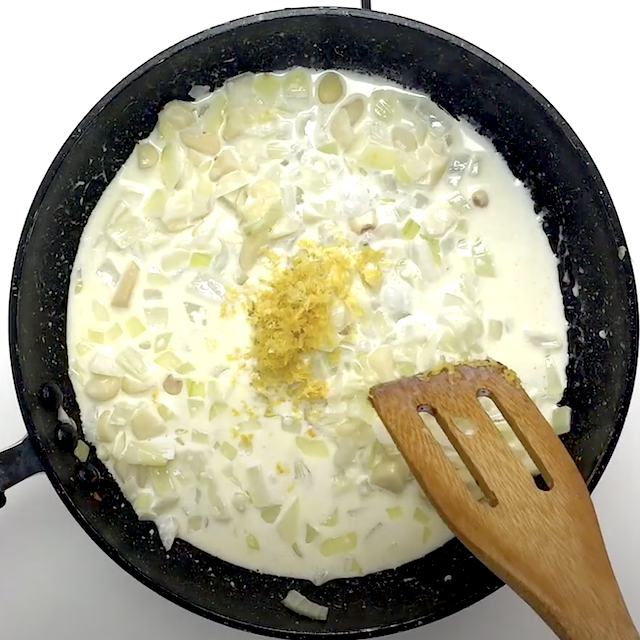 Heavy cream and lemon zest being added to sautéed aromatics to make lemon salmon pasta.