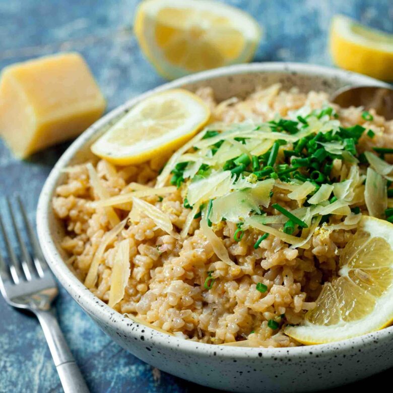 A bowl of instant pot risotto topped with grated cheese and chopped herbs, with lemon wedges placed around it. 