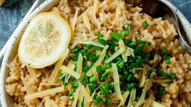 Overhead shot of a bowl of risotto garnished with lemon slices, grated cheese, and chopped herbs.