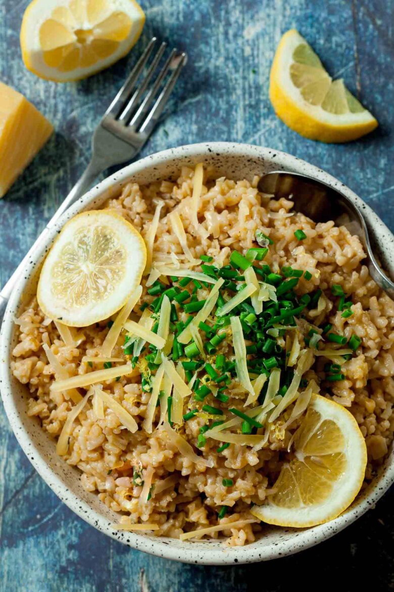 Overhead shot of a bowl of risotto garnished with lemon slices, grated cheese, and chopped herbs.
