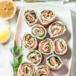 Overhead shot of smoked salmon pinwheels on a rectangular serving dish.