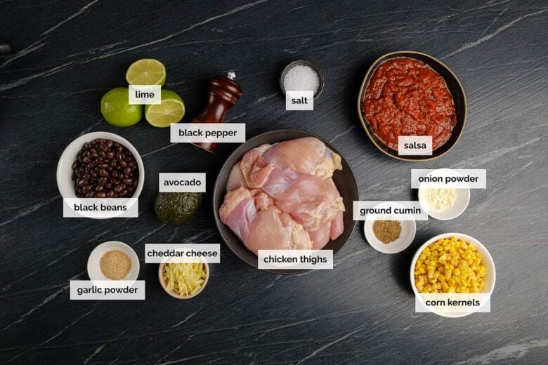 Overhead shot of ingredients to make crockpot salsa chicken at home on a dark surface.