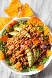 Overhead shot of dorito taco salad drizzled with homemade thousand-island based dressing and garnishes.