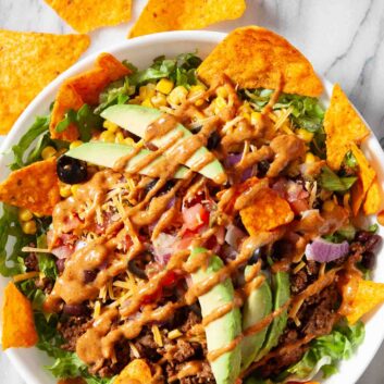 Overhead shot of dorito taco salad drizzled with homemade thousand-island based dressing and garnishes.