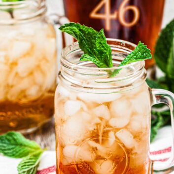 Two mason jar glasses filled with icy mint julep, garnished with mint sprigs.