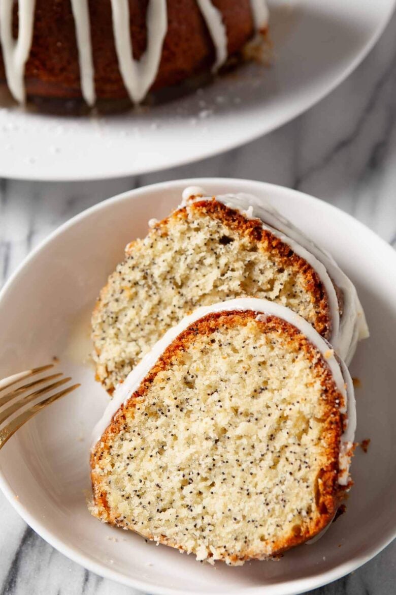 Overhead shot of two slices of poppy seed cake with icing on a white plate.