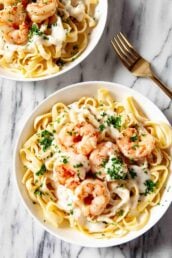 Overhead shot of shrimp alfredo in a while plate, garnished with freshly chopped herbs.