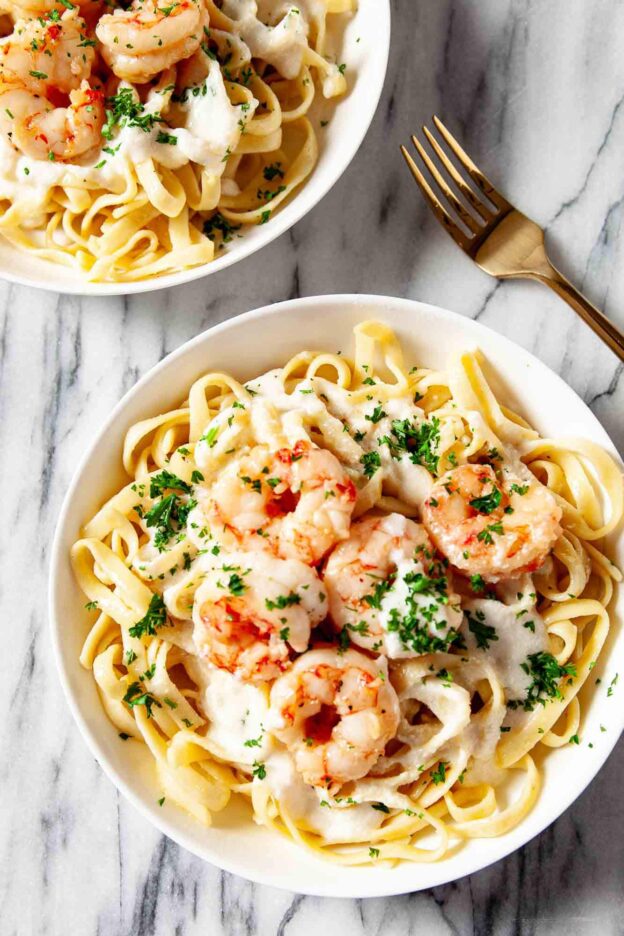 Overhead shot of shrimp alfredo in a while plate, garnished with freshly chopped herbs.