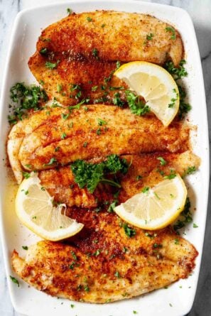 Overhead shot of crispy air fryer tilapia with chopped herbs and lemon wedges.