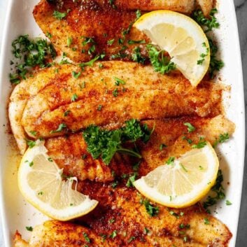 Overhead shot of crispy air fryer tilapia with chopped herbs and lemon wedges.