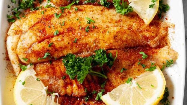 Overhead shot of crispy air fryer tilapia with chopped herbs and lemon wedges.
