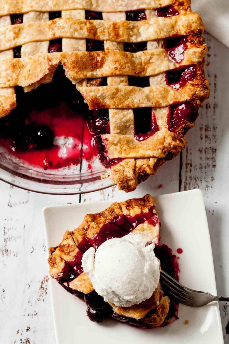 Overhead shot of a slice of sweet cherry pie with a scoop of vanilla ice cream on top and the rest of the pie on the side.