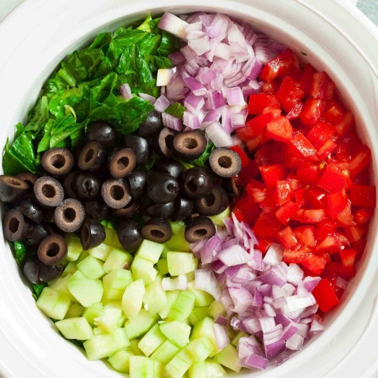 Overhead shot of ingredients to make chopepd greek salad in a bowl.