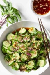 Overhead shot of Asian cucumber salad with chopped onions and herbs visible, and chopsticks on the side.