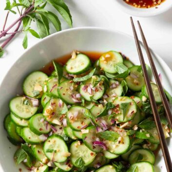 Overhead shot of Asian cucumber salad with chopped onions and herbs visible, and chopsticks on the side.