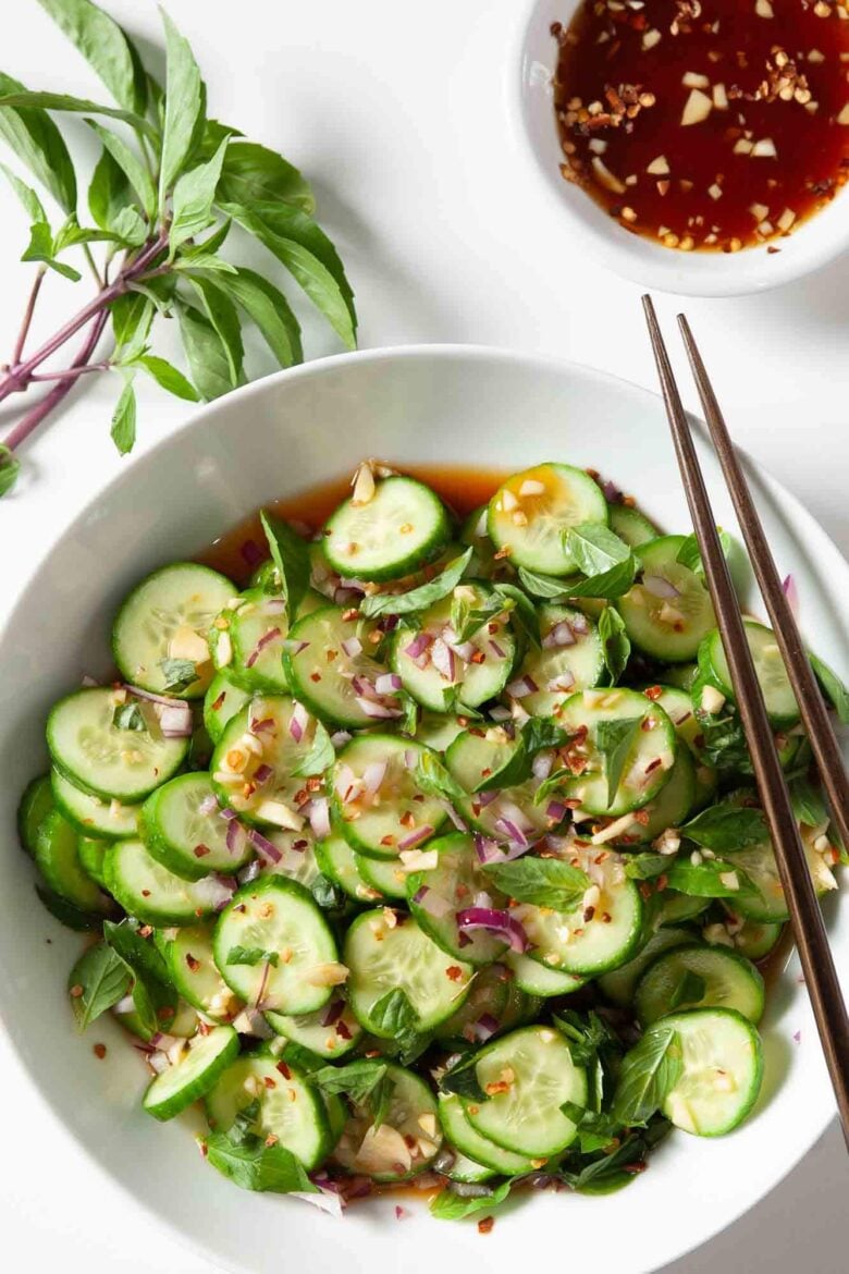 Overhead shot of Asian cucumber salad with chopped onions and herbs visible, and chopsticks on the side.