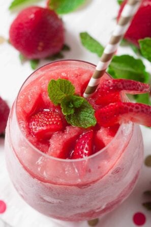 A glass of strawberry frosé made using a classic frosé recipe, topped with fresh strawberry slices and mint leaves, served with a striped straw.