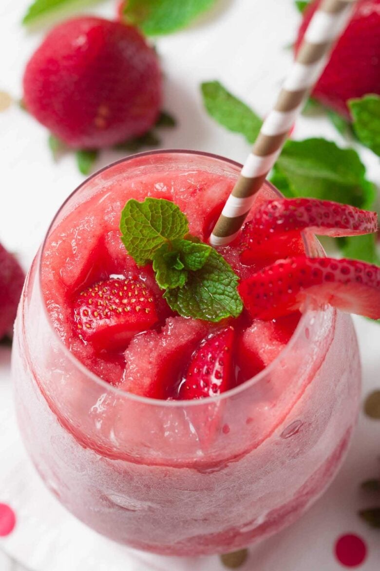 A glass of strawberry frosé made using a classic frosé recipe, topped with fresh strawberry slices and mint leaves, served with a striped straw.