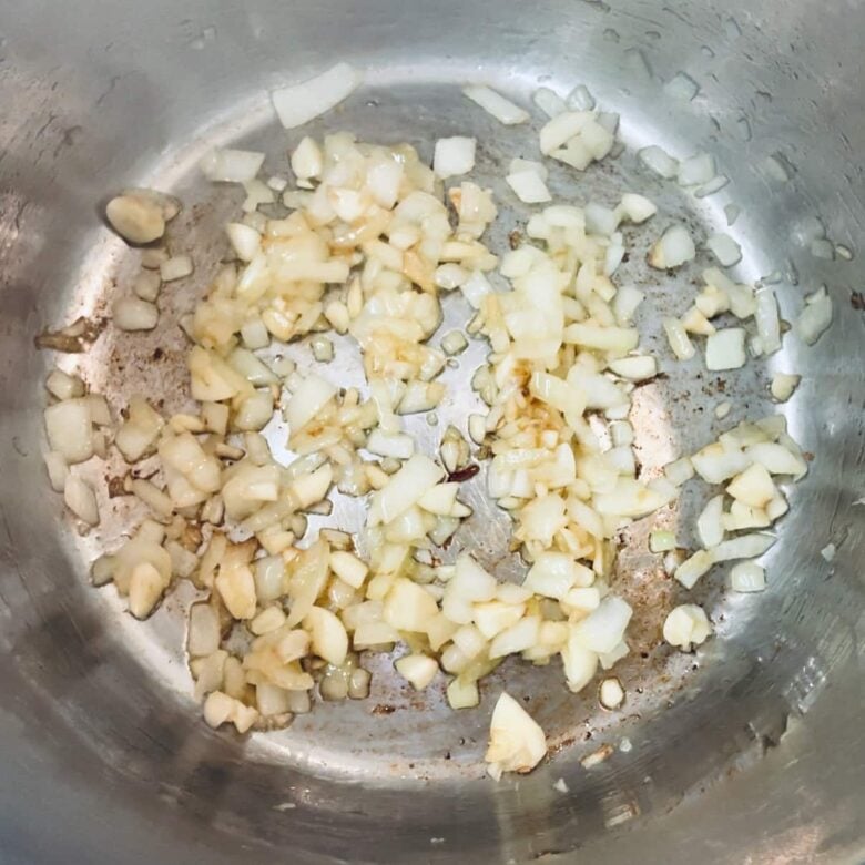 Overhead shot of chopped onions and garlic being sautéed in an instant pot to make mexican rice.