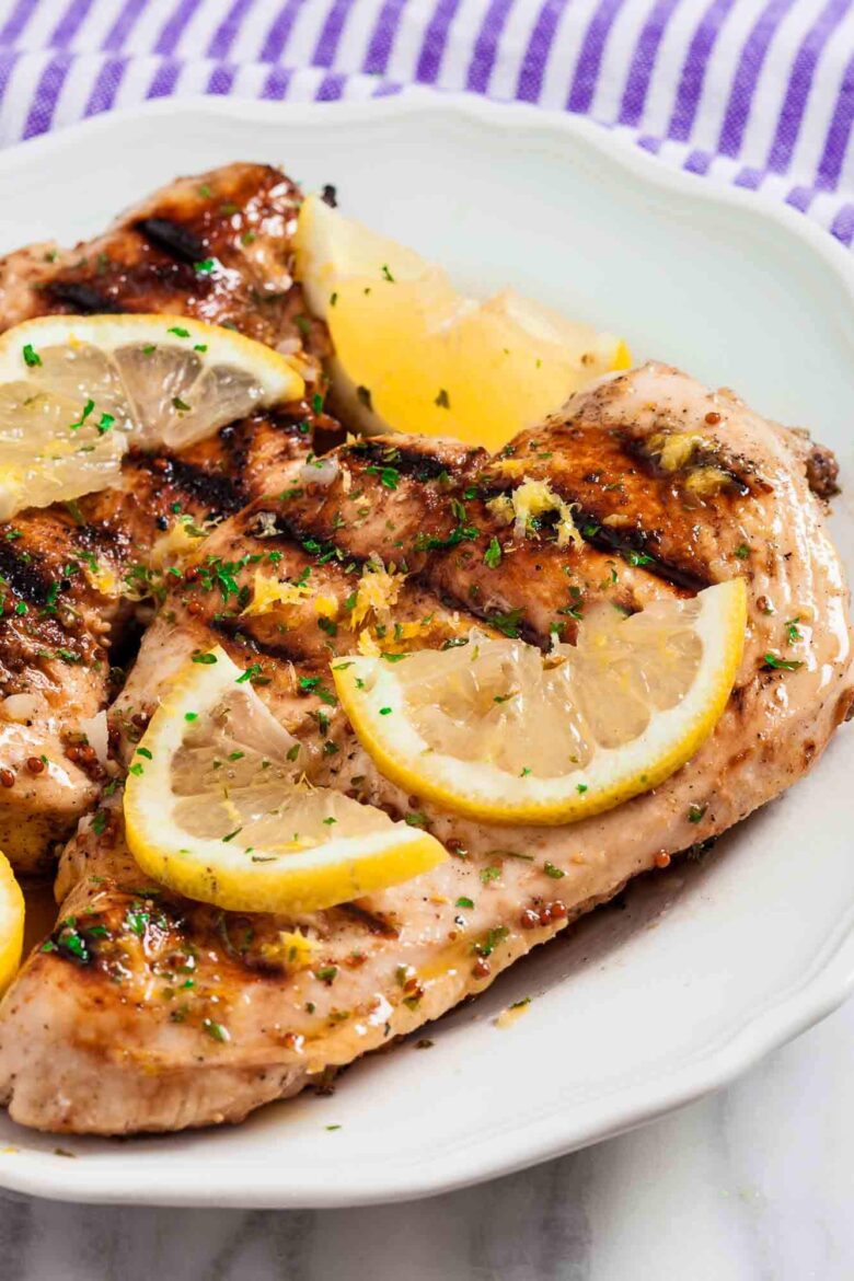 Grilled lemon chicken with sliced lemon wedges on top and chopped herbs.