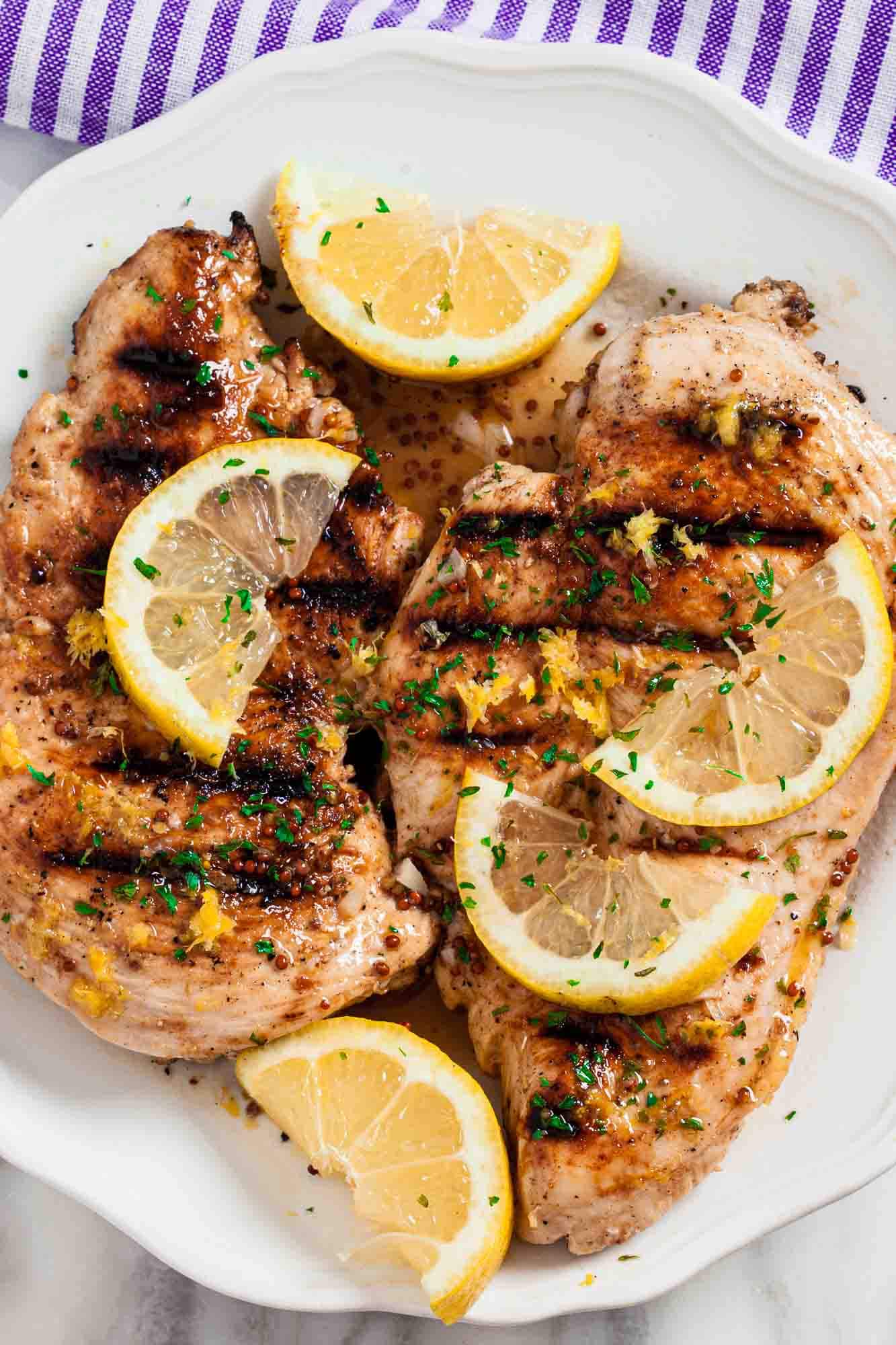 Overhead shot of grilled lemon chicken with sliced lemon wedges on top and chopped herbs.