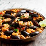 Easy seafood paella in a pan with cooked mussels, clams, and shrimp. Served with lime wedges.
