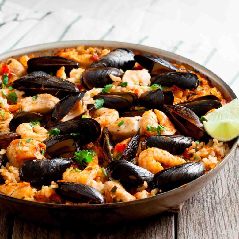 Easy seafood paella in a pan with cooked mussels, clams, and shrimp. Served with lime wedges.