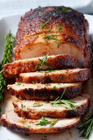 Sliced tender smoked pork loin garnished with fresh rosemary on a white plate.