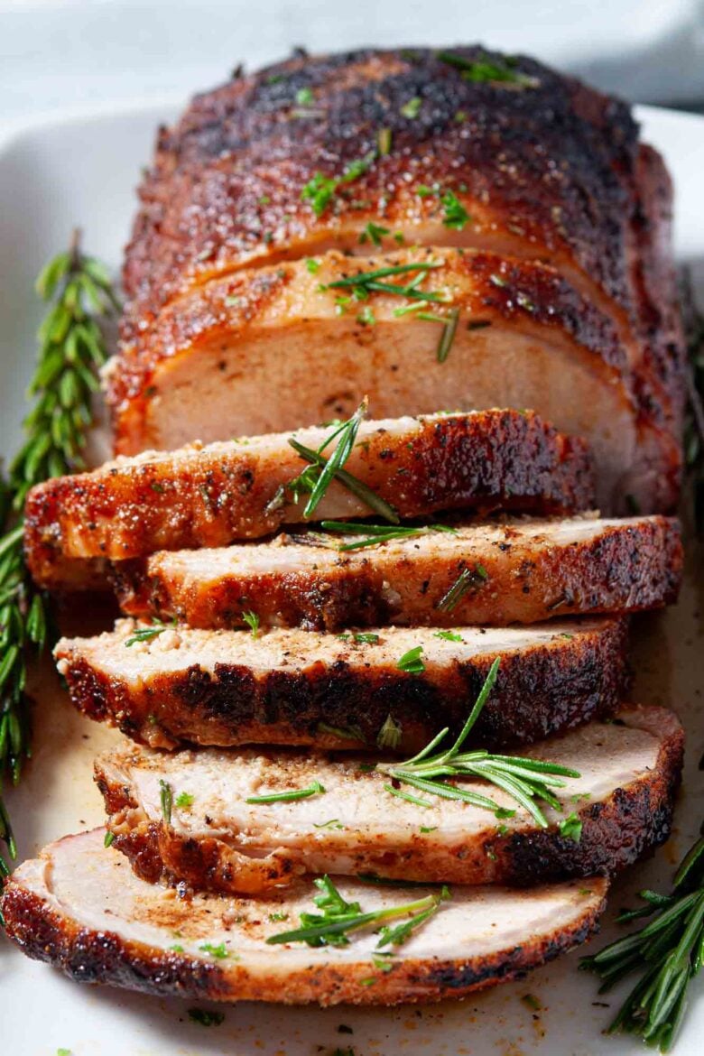 Sliced tender smoked pork loin garnished with fresh rosemary on a white plate.
