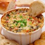 Freshly baked spinach artichoke dip without mayo with a baguette slice in it.