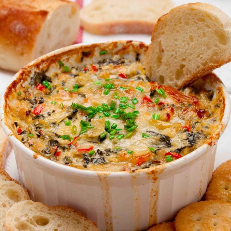 Freshly baked spinach artichoke dip without mayo with a baguette slice in it.