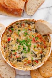 Overhead shot of freshly baked spinach artichoke dip without mayo with a baguette slice in it.