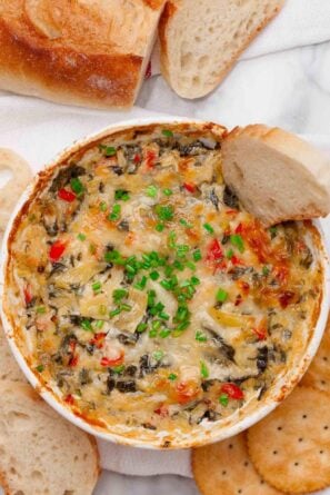 Overhead shot of freshly baked spinach artichoke dip without mayo with a baguette slice in it.