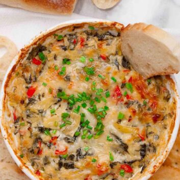 Overhead shot of freshly baked spinach artichoke dip without mayo with a baguette slice in it.