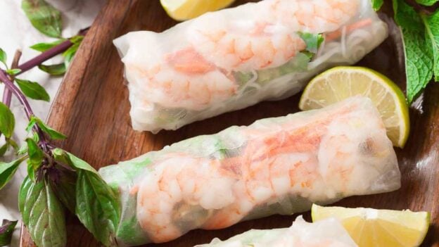 Three freshly made Vietnamese spring rolls with lime wedges on the side.