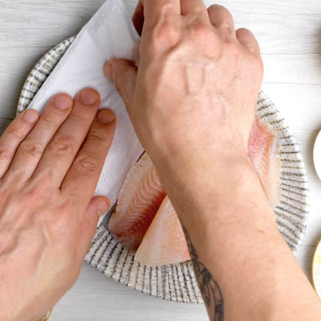 Tilapia fillets being patted dry to make air fryer tilapia at home.