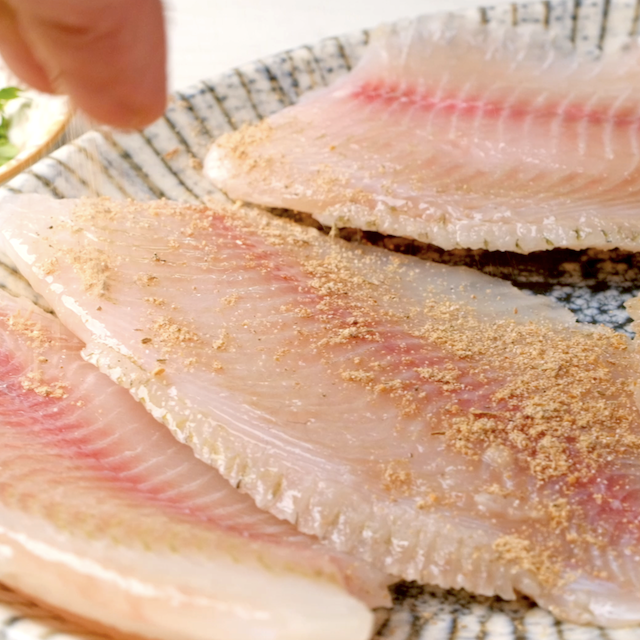 Seasonings being sprinkled on top of tilapia fillets to make air fryer tilapia.