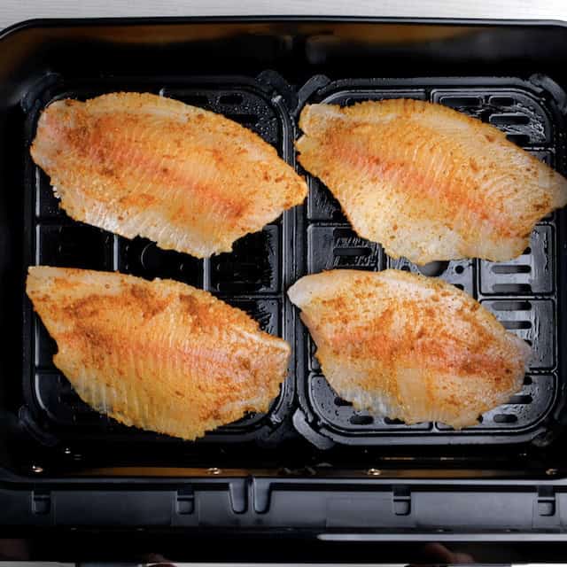 Seasoned tilapia fillets in an air fryer basket ready to be air fried to make air fryer tilapia at home.