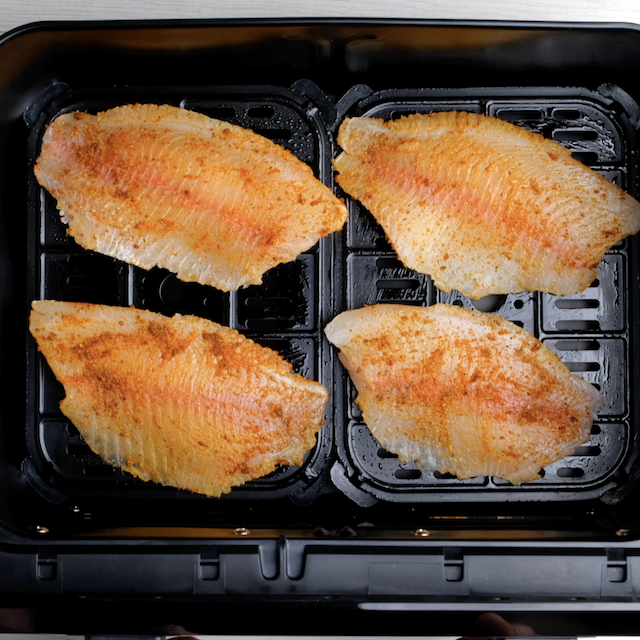Seasoned tilapia fillets in an air fryer basket ready to be air fried to make air fryer tilapia at home.