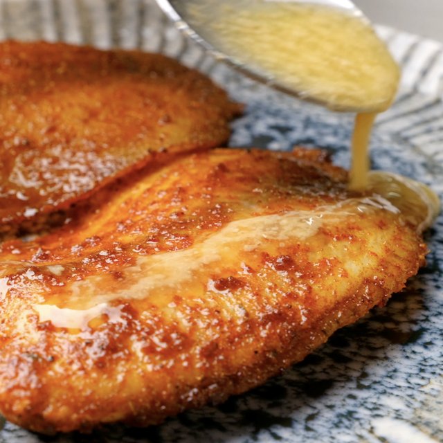 Sauce being drizzled over freshly air fried tilapia fillet to make air fryer tilapia at home.