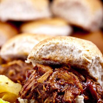 Close-up of a BBQ Pulled Chicken sandwich made in the crock pot, served on a burger bun with barbecue sauce.