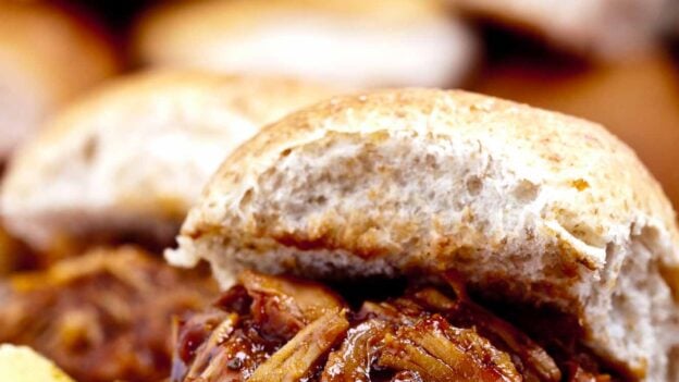 Close-up of a BBQ Pulled Chicken sandwich made in the crock pot, served on a burger bun with barbecue sauce.