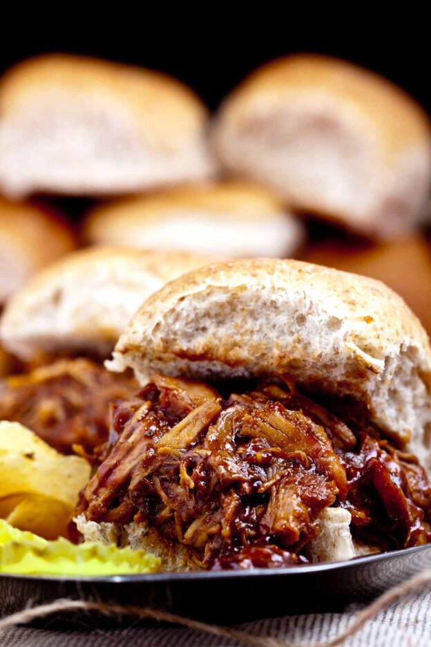 Close-up of a BBQ Pulled Chicken sandwich made in the crock pot, served on a burger bun with barbecue sauce.